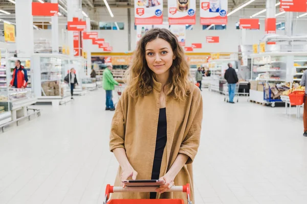Business nainen tabletti seisoo ostoskorin supermarketissa — kuvapankkivalokuva