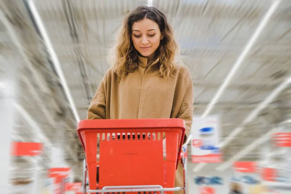 Nuori nainen, jolla on ostoskärry ja joka katselee taulua supermarketissa — kuvapankkivalokuva