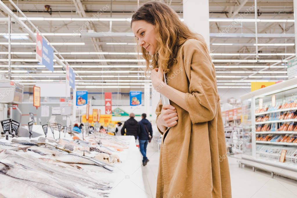 Young woman with a tablet picks fish in a supermarket