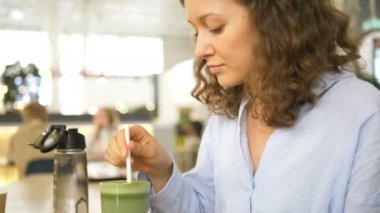 Bir kadın bir kafede pipetle bir bardaktan smoothie içer.