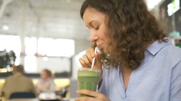 Hermosa chica rizada bebiendo batido verde en patio de comidas — Vídeos de Stock