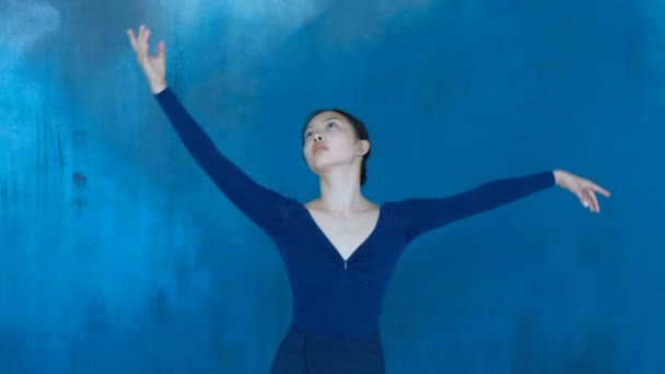 Профессиональная балерина танцует чувственно, делает плавные движения руками на синем фоне — стоковое видео