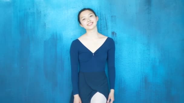 Happy Asian ballerina girl laughs and looks at camera on blue background — Stockvideo