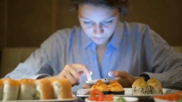 Menina surfa redes sociais na frente de pratos com sushi — Vídeo de Stock