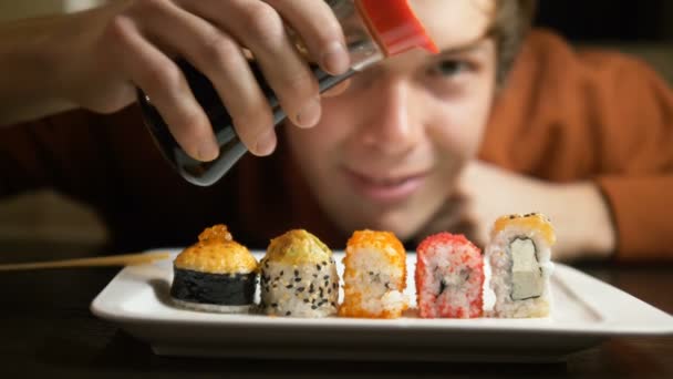 Mann gießt Sojasauce auf köstliches Sushi verschiedener Sorten — Stockvideo