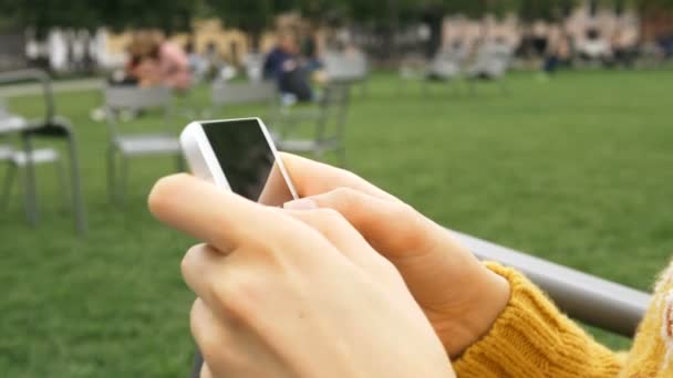 Flicka händer med gula ärmar hålla vit smartphone i parken — Stockvideo