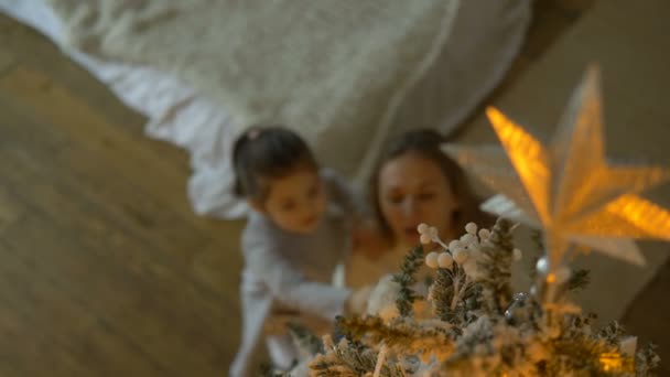 Mãe abraços criança admirando árvore de Natal com topo em primeiro plano — Vídeo de Stock