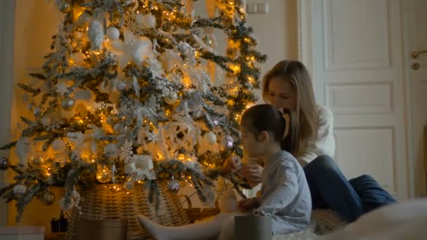 Длинноволосая мама украшает подсвеченную елку у ребенка — стоковое видео