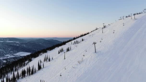 Modern ski resort chairlift moves over tracks against forest — Stock Video