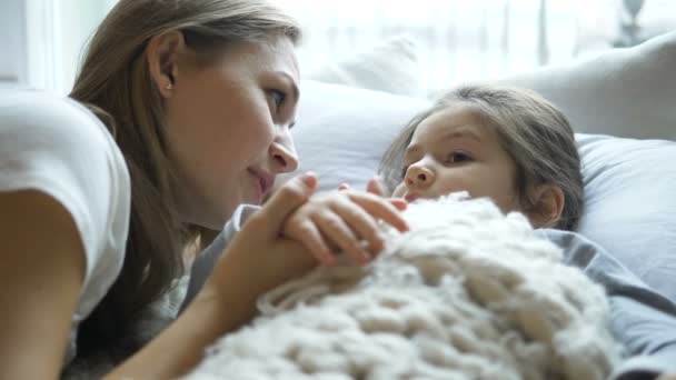 Счастливая любящая мать рассказывает историю своей маленькой дочери в постели — стоковое видео