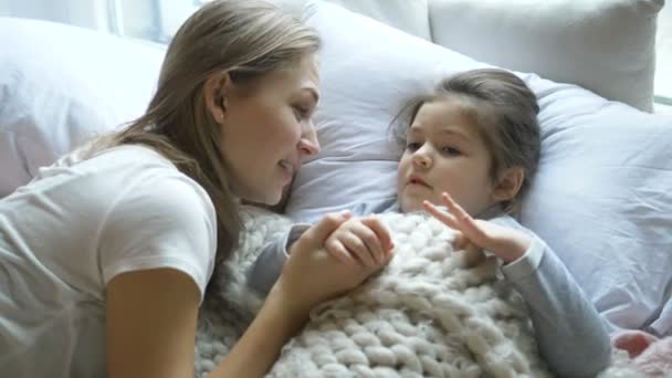 Леди с светлыми волосами разговаривает с маленьким ребенком под одеялом — стоковое видео