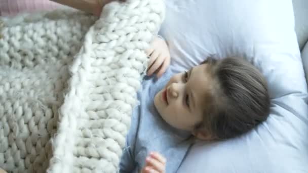Νεαρή μητέρα τυλίγει το παιδί με λευκή κουβέρτα στο κρεβάτι closeup — Αρχείο Βίντεο