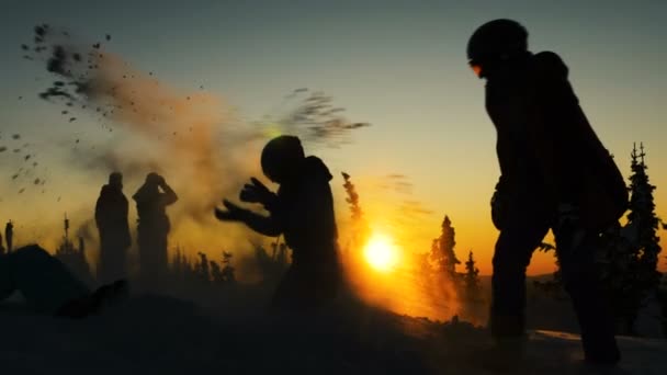Tourist silhouettes throw snow among pine trees at sunset — 비디오