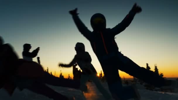 Смішні лижники стрибають у сніг роблячи фотографії проти заходу сонця — стокове відео