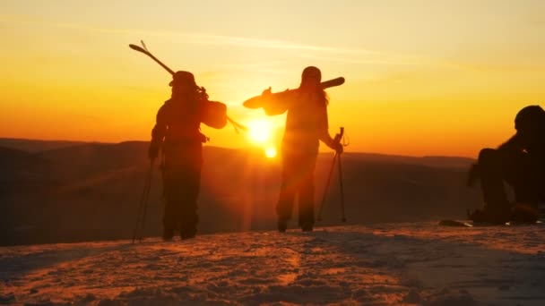 Personer med skidutrustning promenerar längs snöig backe vid solnedgången — Stockvideo