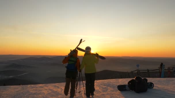 Síelők sétálnak a havas dombtetőn a hegyek ellen naplementekor — Stock videók