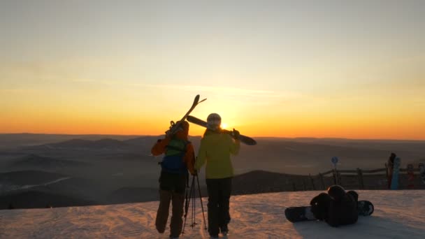 Sciatori a piedi lungo la collina innevata contro le colline al tramonto — Video Stock