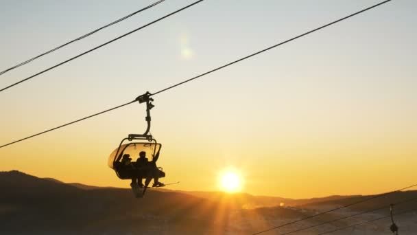 Silhuetas esquiador mover no teleférico contra o pôr do sol disco — Vídeo de Stock