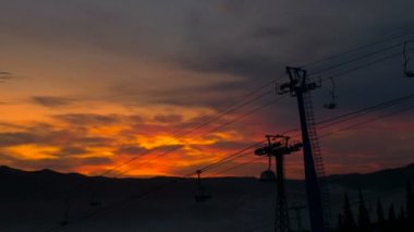 Teleferik kulübeleri akşam gökyüzünün altındaki çam ağaçlarının üzerinde hareket eder.