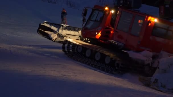 Оранжевый подсвеченный снегоход подъезжает к тёмному снежному холму — стоковое видео