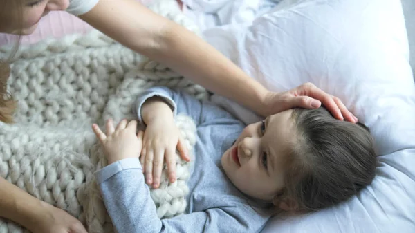 Giovane madre avvolge bambino con coperta bianca sul letto primo piano — Foto Stock