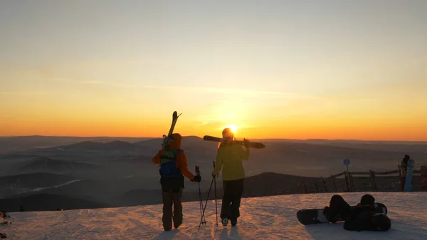 Skifahrer laufen bei Sonnenuntergang auf schneebedecktem Hügel gegen Hügel — Stockfoto