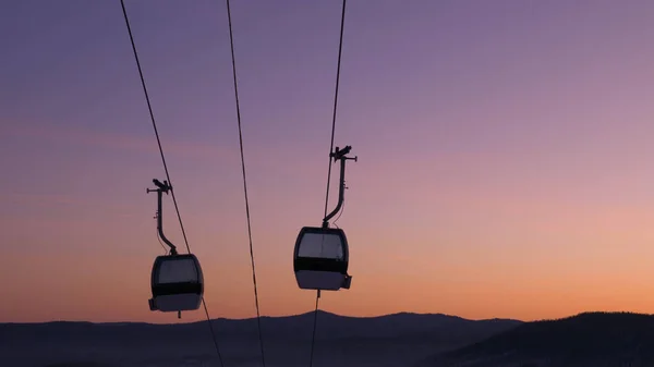 Modern ski lift cabin silhouettes move against sunset sky — Stock Photo, Image