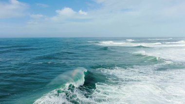 Büyük mavi okyanus dalgaları sprey ve köpükle çarpışarak gökkuşağı ve hava manzarası oluşturur.