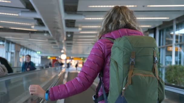 Wanita dalam jaket dengan ransel rides travelator di bandara, gerakan lambat — Stok Video