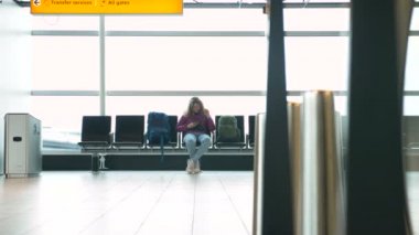 Kadın modern havaalanı binasında akıllı telefondan video izliyor.