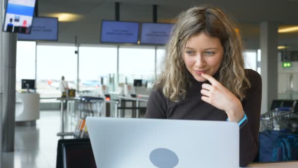 Радісна дівчина працює на ноутбуці, сидячи в кафе в аеропорту — стокове відео