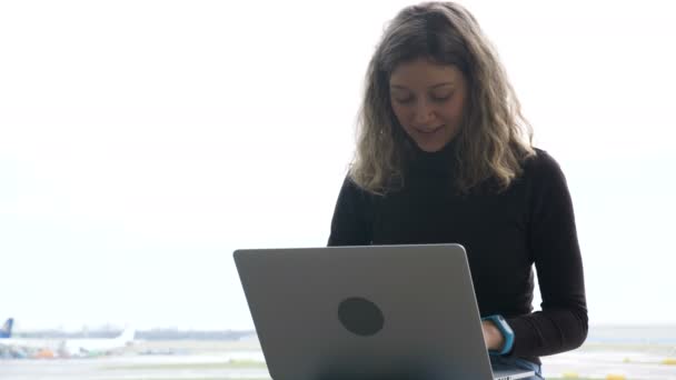 Šťastná dívka surfuje na internetu na notebooku oknem na letišti — Stock video
