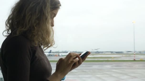 Girl surfs internet with cell phone against airfield at airport — Stock Video