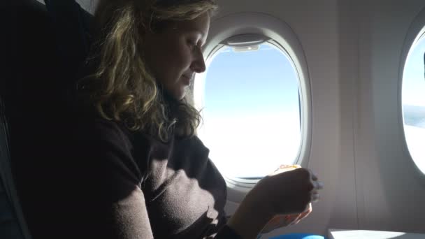 Девушка сидит рядом с иллюминатором и ест торт, путешествуя на самолете — стоковое видео