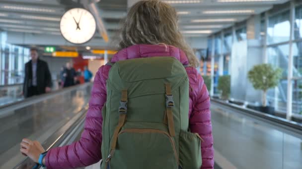 Blondine mit Rucksack fährt am Flughafen auf Umzugswagen auf — Stockvideo