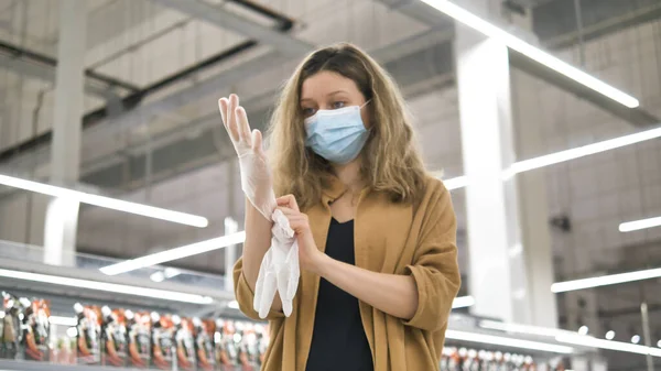 Молода дівчина в супермаркеті одягає захисну медичну маску і гумові рукавички для захисту від зараження коронавірусом . — стокове фото