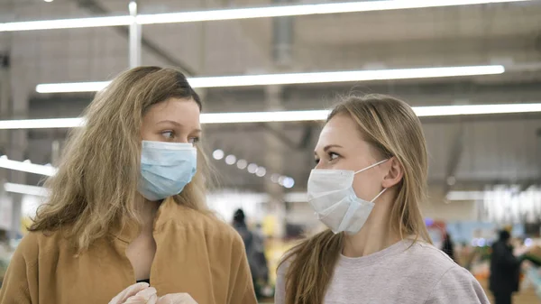 İki bayan arkadaş bir süpermarkette lastik eldiven takıp tıbbi maskeler taktılar. Üzülerek iç çektiler ve birbirlerine baktılar. Koronavirüs salgınıyla mücadele için koruyucu önlemler.