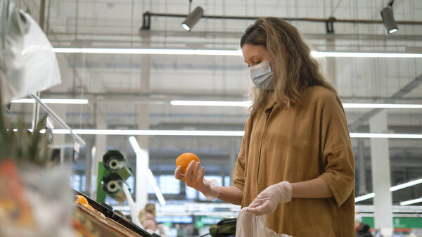 Женщина в медицинской маске и перчатках выбирает апельсины в супермаркете. Защита от эпидемии коронавируса, повышение иммунитета свежими фруктами
.