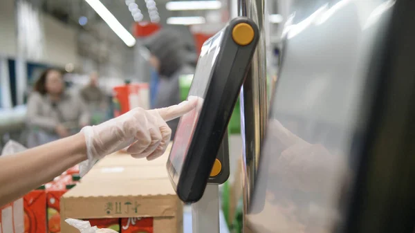 Kadınlar koruyucu eldivenler veriyorlar süpermarkette elektronik ölçekte sebzeleri tartıyorlar, istenen ürünü dokunmatik ekrandan seçiyorlar. Koronavirüse karşı koruyucu önlemler.