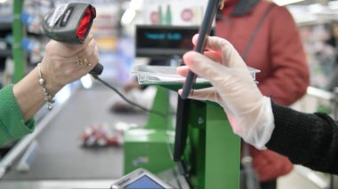 Süpermarketteki kasada duran bir kadın müşteriye akıllı telefonundan lazer alan bir kart veriyor. Coronavirüs kapmamak için süpermarkette koruyucu eldivenlerle ödeme yapmak.