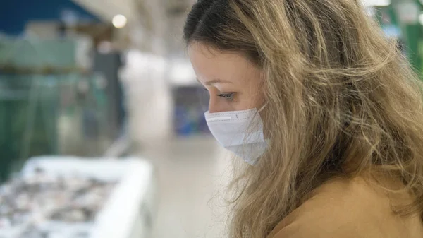 Дівчина в захисній масці ретельно підбирає продукти в супермаркеті, заходи карантинної коровірусної безпеки — стокове фото