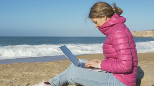 Дама сидит с ноутбуком на пляжном песке и работает серфингистом в Интернете — стоковое видео