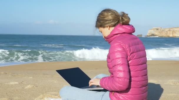 女性はビーチの砂の上にノートパソコンを置き — ストック動画