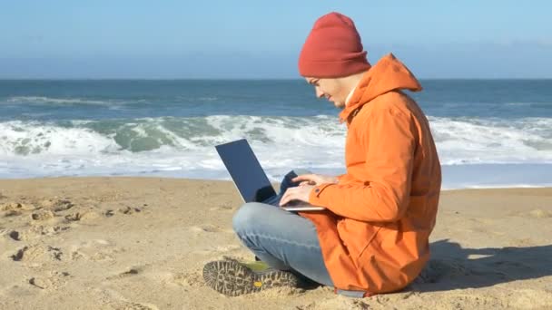 Uomo gode di distanza di lavoro seduto sulla spiaggia di sabbia con computer portatile — Video Stock