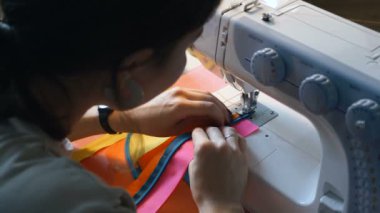 Terzi dikiş makinesiyle kumaş şeritleri dikiyor.