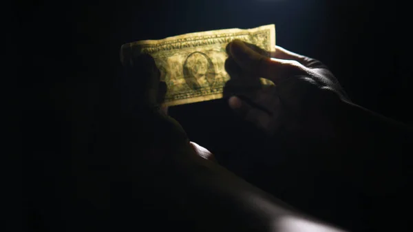 Dolar banknotları karanlığın içinde, ışığın altında bir adamın eline geçer. Adam dolar açar. — Stok fotoğraf