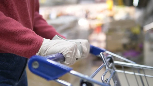 Žena v supermarketu válí vozík s potravinami v gumových rukavicích. Chrání před koronavirem. — Stock fotografie