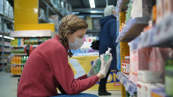 Молода жінка в супермаркеті медичної маски і гумові рукавички вибирають рідке мило, щоб захистити від коронавірусу. Пандемія коронавірусу. — стокове фото