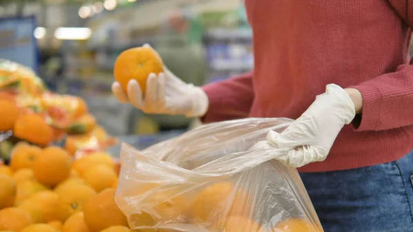 Koruyucu eldivenli kadın portakalları plastik torbaya, C vitamini Coronavirus covid-19 'a koyar.