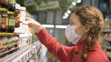 Maskeli ve eldivenli kızın portresi süpermarketteki ürünlerin etiketlerini, kişisel koruma koronavirüsünü gösteriyor.